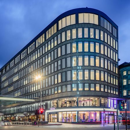 Yotel กลาสโกว์ ภายนอก รูปภาพ The photo shows a modern office building with a distinctive curved shape and a facade made of large glass windows. It is illuminated against a twilight sky, giving it a contemporary appearance. The ground floor features large glass entrance areas, li