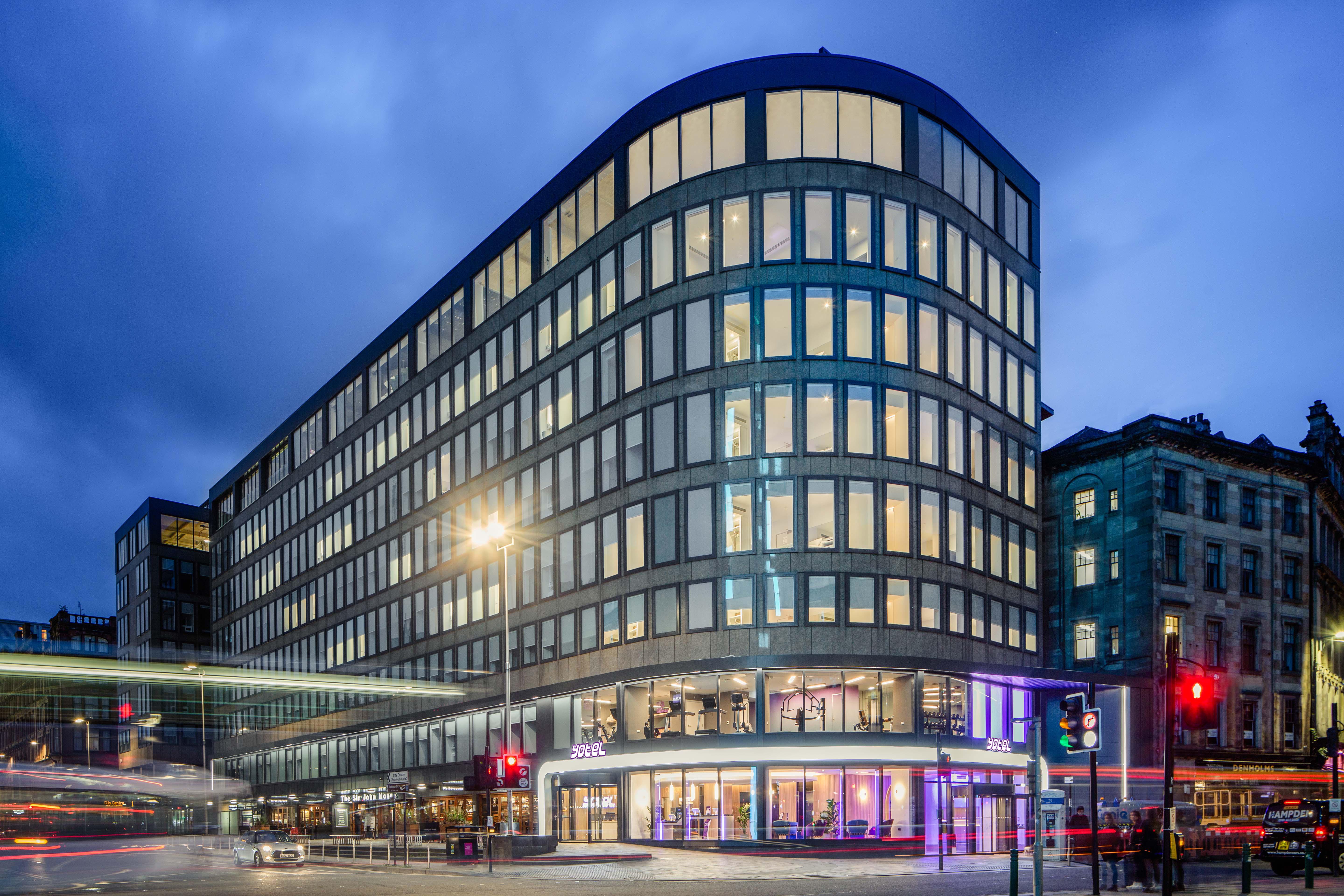 Yotel กลาสโกว์ ภายนอก รูปภาพ The photo shows a modern office building with a distinctive curved shape and a facade made of large glass windows. It is illuminated against a twilight sky, giving it a contemporary appearance. The ground floor features large glass entrance areas, li